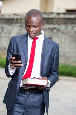 Bir kitap sol elinde tutan ve bir cep telefonu diğer el ile düzenleme genç öğrenci