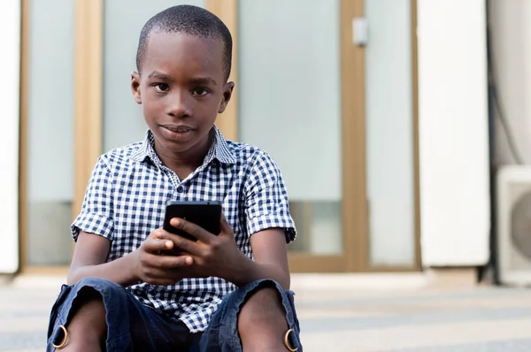Little boy sitting with a mobile phone in his hands and looking at the camera.