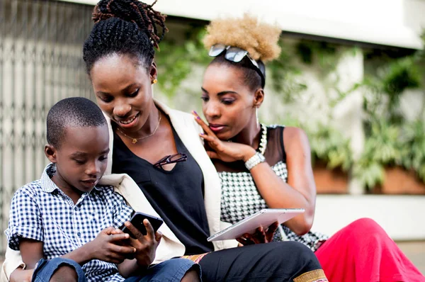 Young women amazed by the mastery of the mobile phone by a little boy sitting beside them.