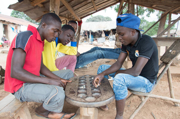 Anekro, Ivory Coast - 27 August 2015: young playing the awal under a shed in the village. Four young men sitting under a shed in the morning indulge in a competition awale games