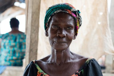 Abican, Fildişi Sahili - 22 Şubat 2017: çok renkli bir eşarp tarafından bağlı ve manyok un, içeren bir tepsi tutarak başını bir taburede oturan Afrikalı kadın kameraya benziyor. Tam attit, tüm Ivorians tarafından sevilen gıda üretimini mevcuttur