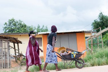 Abican, Fildişi Sahili - 22 Şubat 2017: çok renkli bir eşarp tarafından bağlı ve manyok un, içeren bir tepsi tutarak başını bir taburede oturan Afrikalı kadın kameraya benziyor. Tam attit, tüm Ivorians tarafından sevilen gıda üretimini mevcuttur