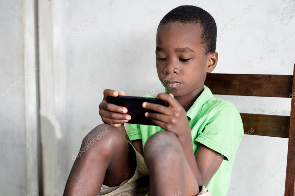 A child sitting on a chair is playing games in a mobile phone.