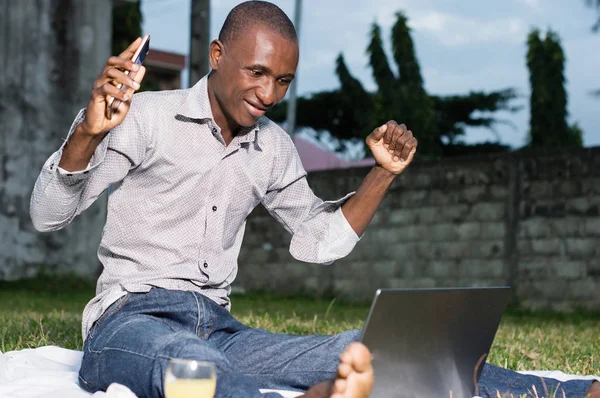 Businessman sitting in garden looking joyfully at his laptop