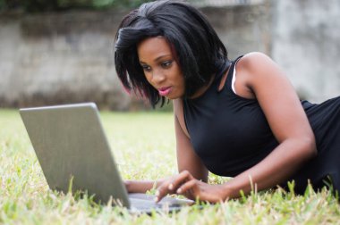 Genç kadınla çimenlerin üzerine yalan onu laptop odaklanmıştır.