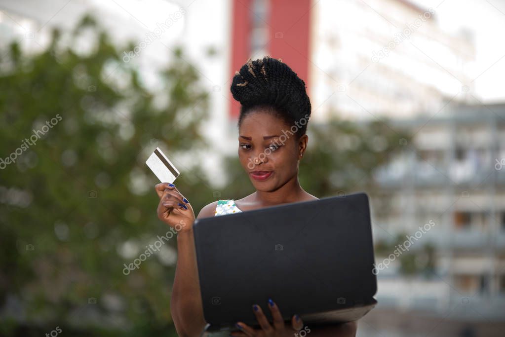 Smiling and confident businesswoman doing online shopping through a laptop and a credit card standing in the street