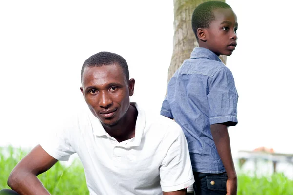 Молодий чоловік сидить на траві зі своїм маленьким братом . — стокове фото