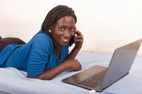 Woman talking on the phone in bed in front of a laptop. — Stock Photo, Image