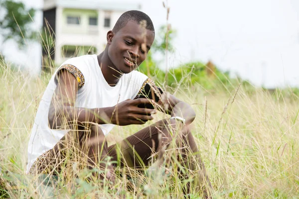 Retrato de un joven sentado en la hierba con un teléfono móvil — Foto de Stock
