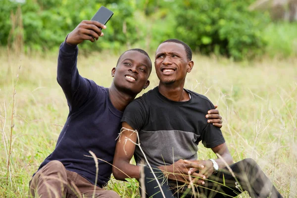 Iki genç kişi çim oturan cep telefonu kullanarak — Stok fotoğraf