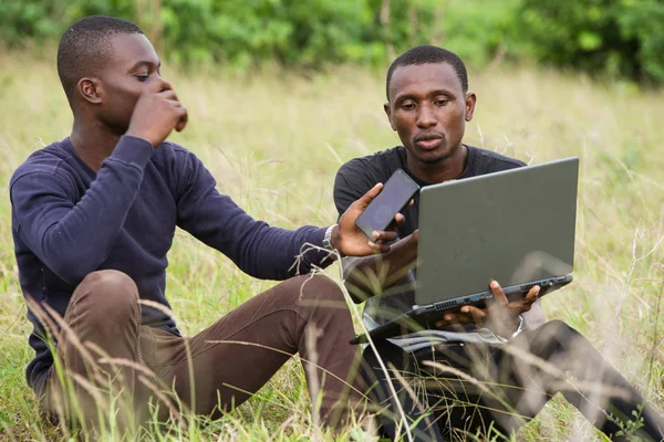 Два молодых человека сидят в парке и разговаривают перед ноутбуком — стоковое фото