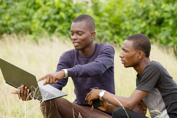 Двое молодых людей работают над ноутбуком на открытом воздухе — стоковое фото