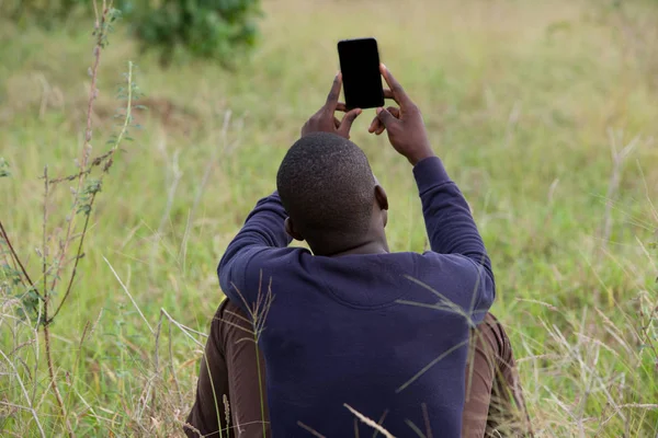 Jovem sentado na grama no parque com um telefone na mão — Fotografia de Stock