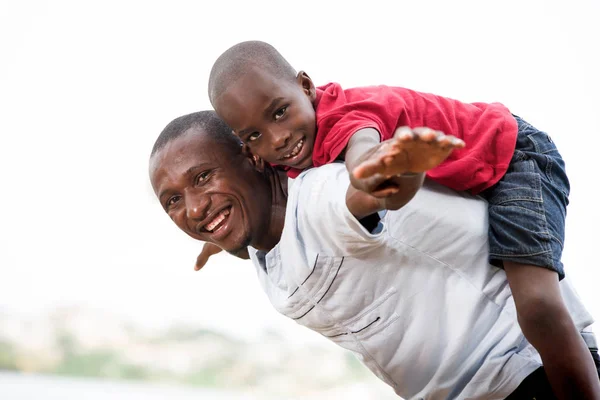 Νεαρό πατέρα που κουβαλάει το γιο του χαμογελώντας στην πλάτη — Φωτογραφία Αρχείου