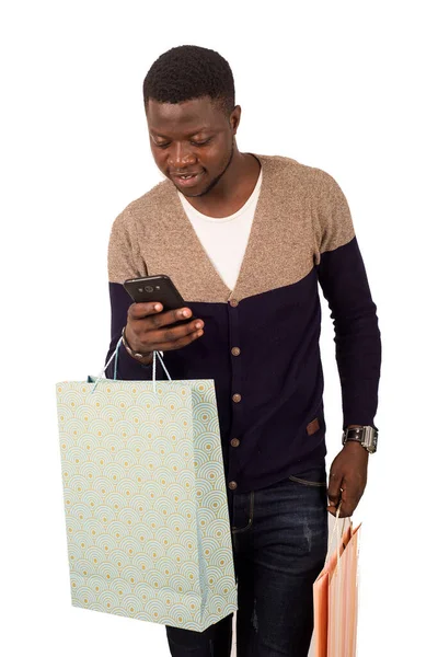 Joven hombre sonriente con bolsas de compras está utilizando un teléfono móvil — Foto de Stock