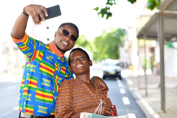 Casal feliz segurando sacos de compras tirando uma foto com um mobil — Fotografia de Stock