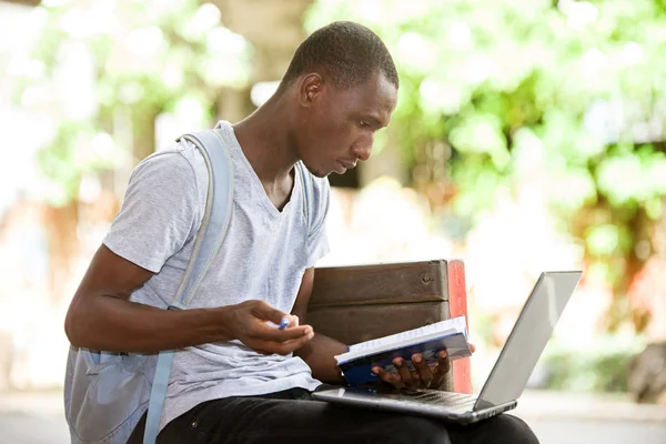 Молодой студент, сидящий в городе и работающий с ноутбуком — стоковое фото