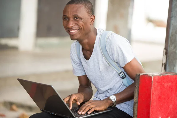 young student man sitting in city working with laptop