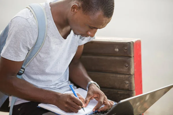 Mladý muž student sedí ve městě pracuje s notebookem a noteb — Stock fotografie