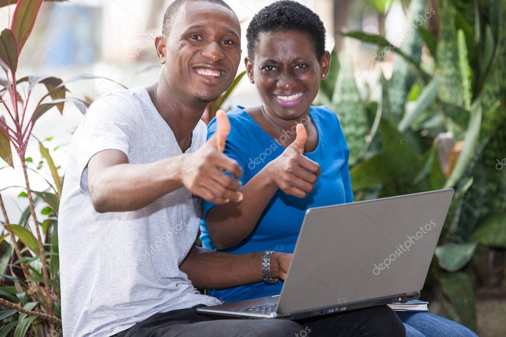 young students sitting in park with laptop showing thumbs up smiling on camera