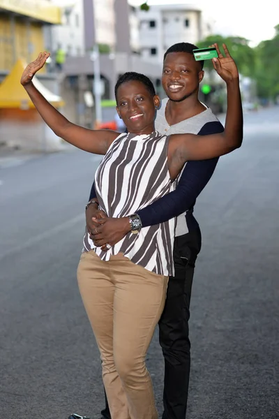 cheerful man embracing from behind happy woman with credit card, happy couple standing in street and looking in camera