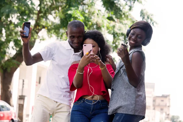 Grupa Trzech Szczęśliwych Młodych Ludzi Telefonem Komórkowym Robi Zdjęcia Słucha — Zdjęcie stockowe