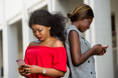 İki genç gülümseyen kadın dışarıda dikilip telefonda konuşuyorlar. Konsept iletişim ve gençlik.