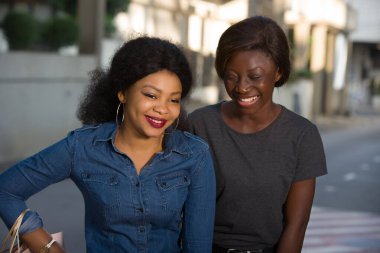 Bir grup gülümseyen kadın kentte birlikte durup alışveriş torbalarını tutuyorlar.