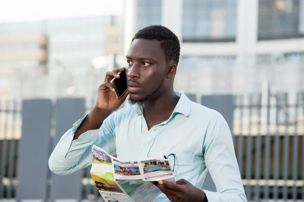 Portrait of modern man holding a card and talking on the phone visiting the city street,