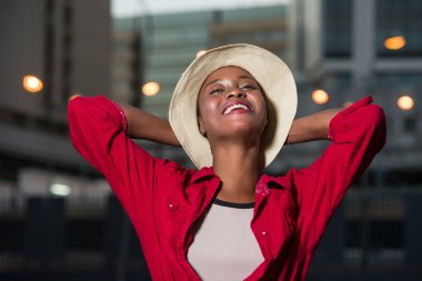 Genç Afrikalı kadın, kırmızı ceketli, bej şapkalı, gülüyor..