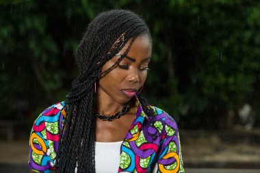 Genç Afrikalı bir kız hafif bir yağmurun altında dikilip bir şeye bakıyor..