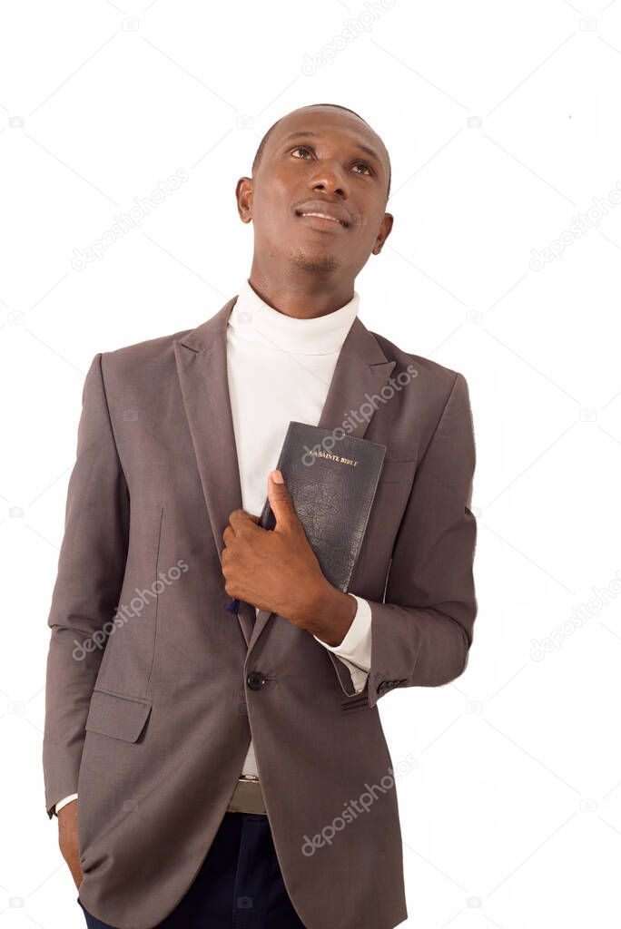 young smiling pastor standing in jacket and holding a Bible on white background.