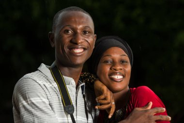 Genç bir çift kamerayla dışarıda dikiliyor ve gülümsüyor..