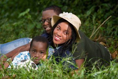 Genç bir aile parkta uzanmış, gülümseyen kamerayı izliyor..