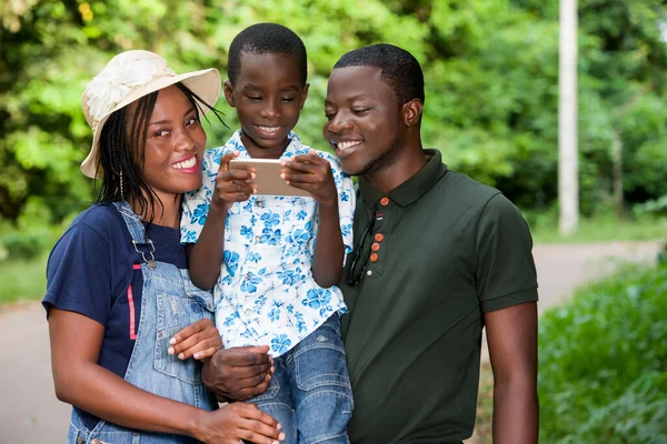 Μια Ευτυχισμένη Οικογένεια Στέκεται Ένα Πάρκο Βλέποντας Κινητό Τηλέφωνο Γιο — Φωτογραφία Αρχείου