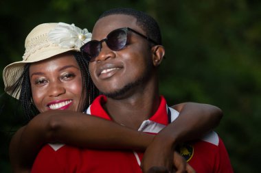 Genç bir çift, kucaklaşan parkta durup gülümsüyor..