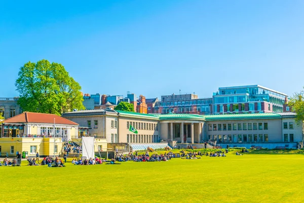 Students are having a picnic on a field inside of the trinity college in Dublin, Irelan