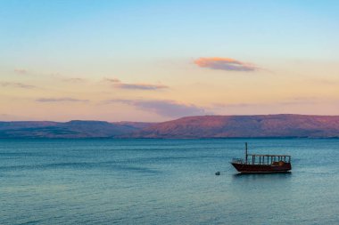 Sunset view of a wooden boat floating on the sea of galilee, Isr clipart