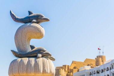 Arka planda bir kale ile Bir Muttrah corniche üzerinde bir yunus heykeli, Muscat, Umman.