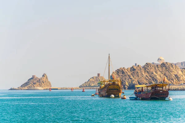 一对单船 - 传统的阿拉伯船只 - 正从马斯喀特的穆特拉部分驶向大海，由阿曼山上的一个要塞控制. — 图库照片