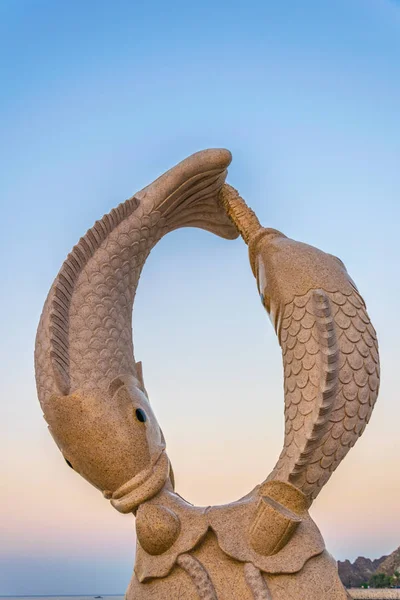 Statua di due pesci su una corniche Muttrah con una fortezza sullo sfondo, Moscato, Oman . — Foto Stock