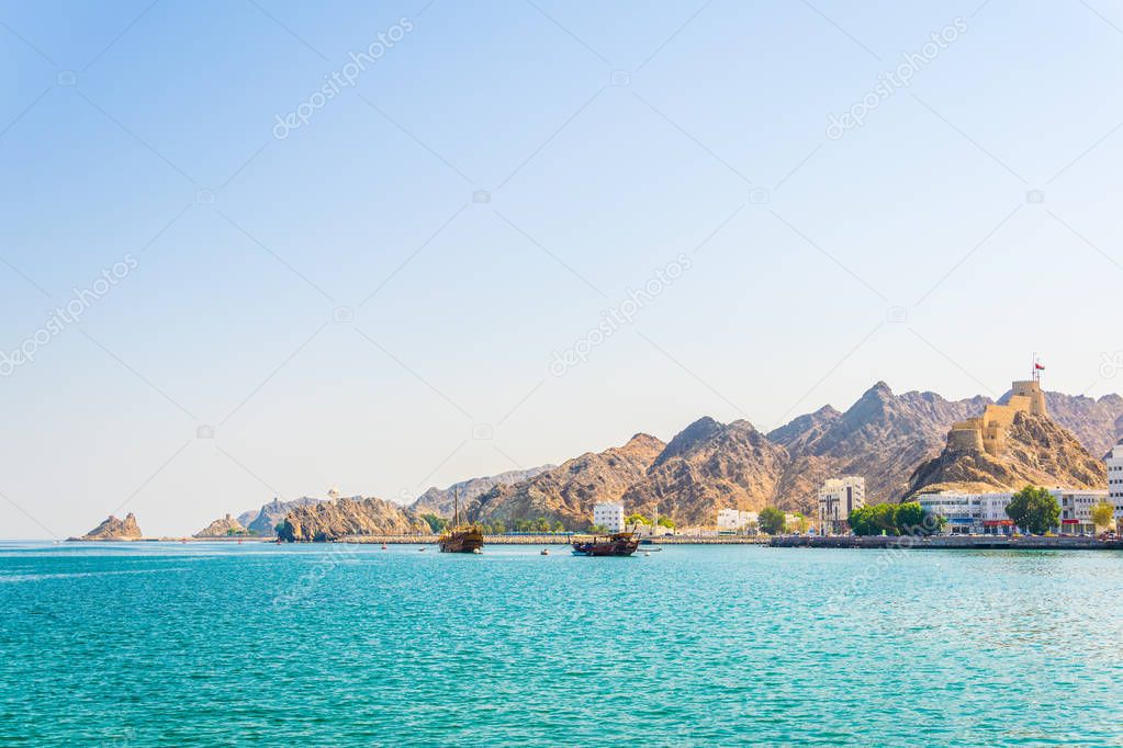 a pair of dhows - traditional arab ships - is heading to the sea from Muttrah part of Muscat dominated by a fort on a hill, Oman.