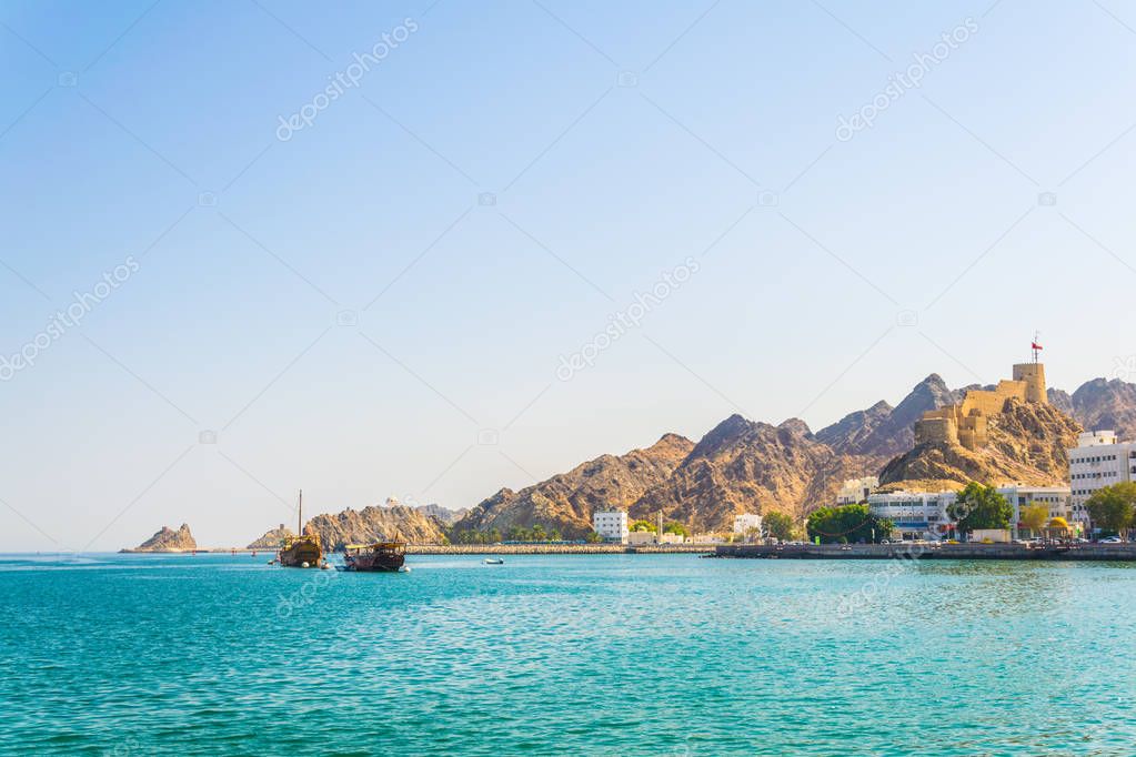 a pair of dhows - traditional arab ships - is heading to the sea from Muttrah part of Muscat dominated by a fort on a hill, Oman.
