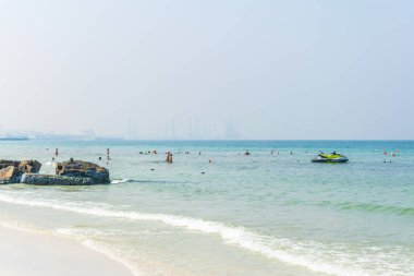 İnsanlar Ajman'da bir plajda yüzüyor ve arka planda Dubai'ye bakıyorlar..