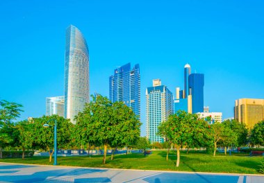 Abu Dabi'de yüksek gökdelenlerle dolu iş merkezinin yanında uzanan bir korniş in manzarası.