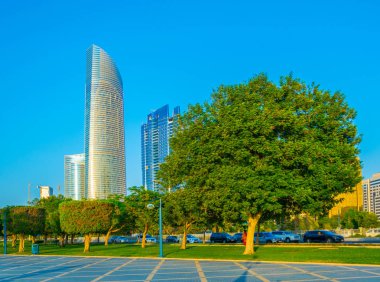 Abu Dabi'de yüksek gökdelenlerle dolu iş merkezinin yanında uzanan bir korniş in manzarası.