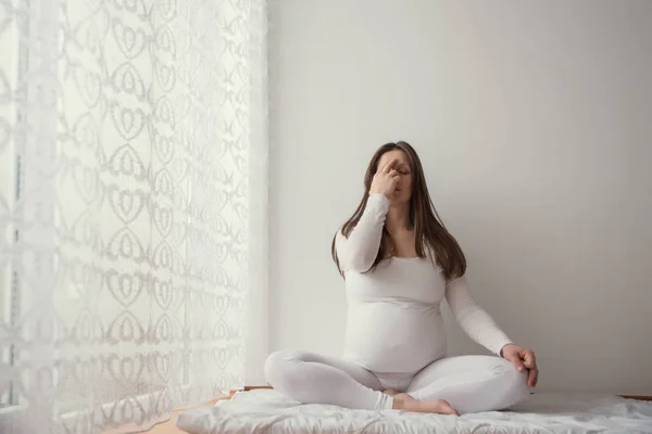 Pregnant woman doing yoga in the room by the window