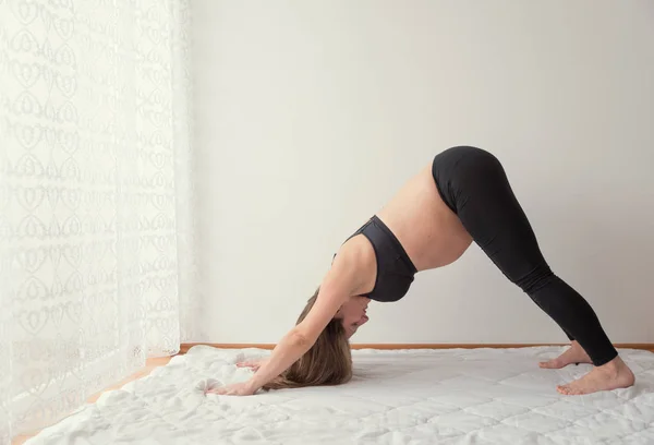 Pregnant woman doing yoga in the room by the window