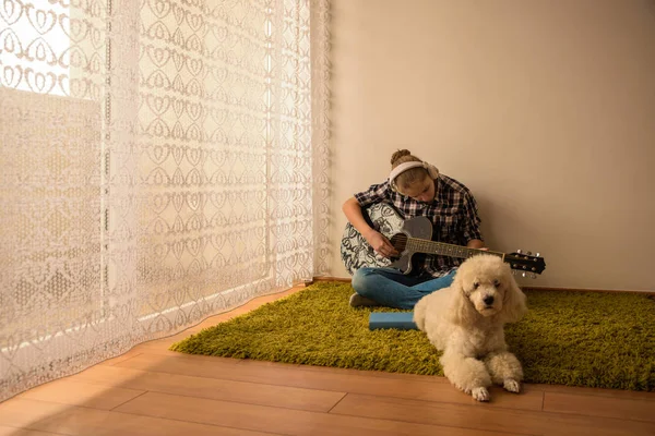 十几岁的人坐在地板上和一只狗一起弹吉他 — 图库照片