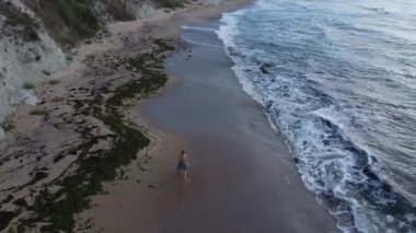 Kumsalda bir kadın yürüyor, uzaktan kumandalı bir uçak.